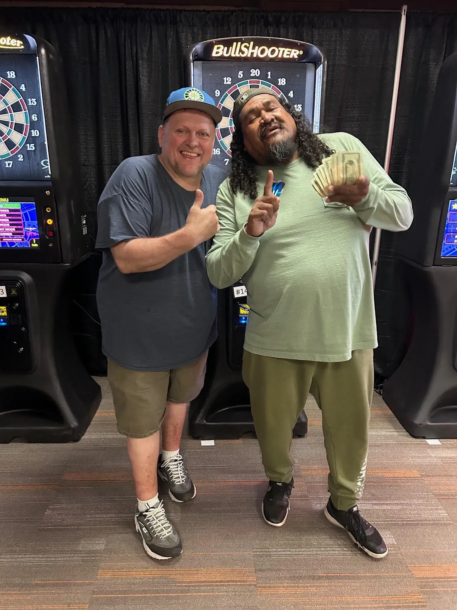 Two men smiling by dart machines