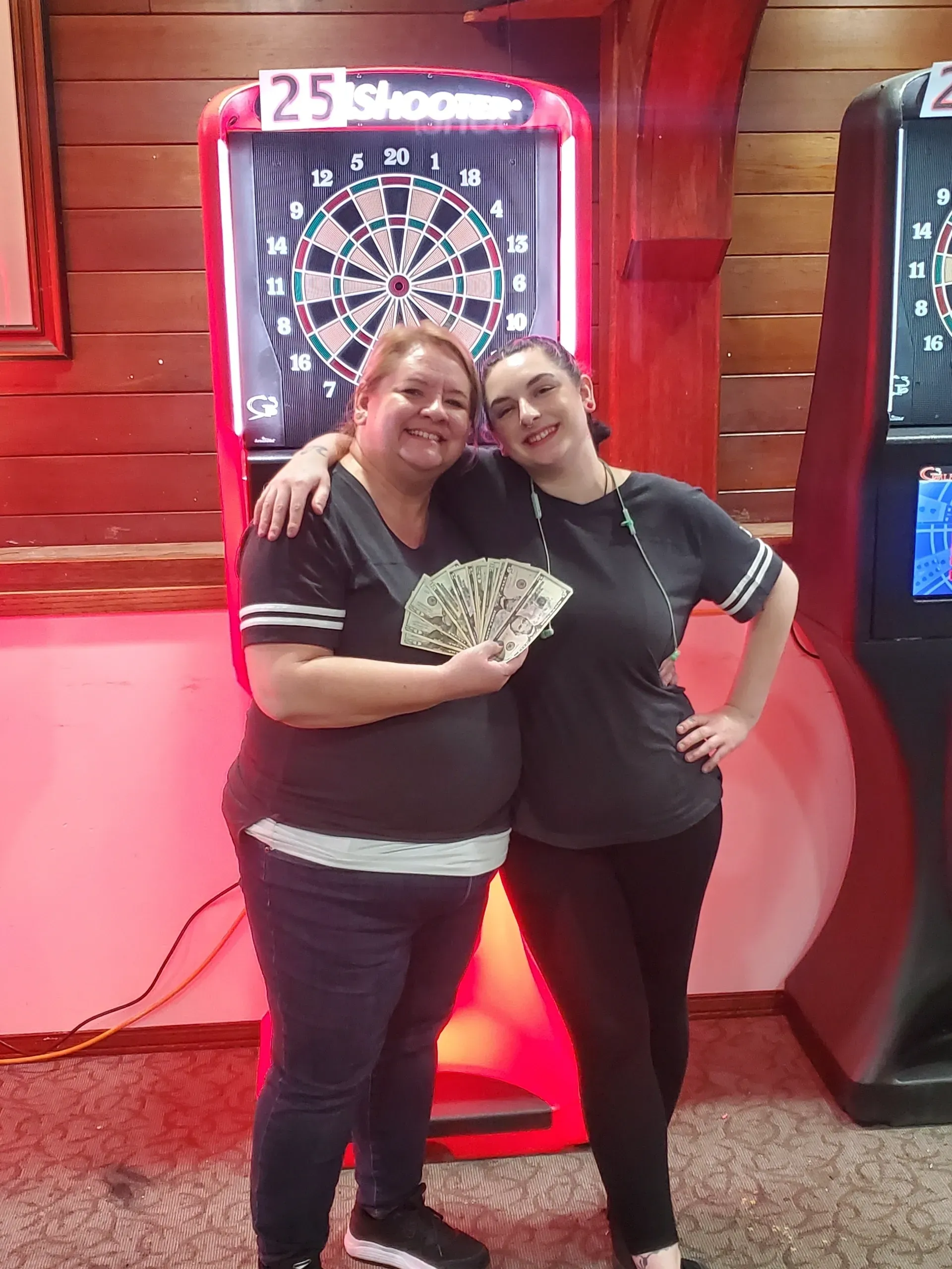 Two people smiling by dartboard