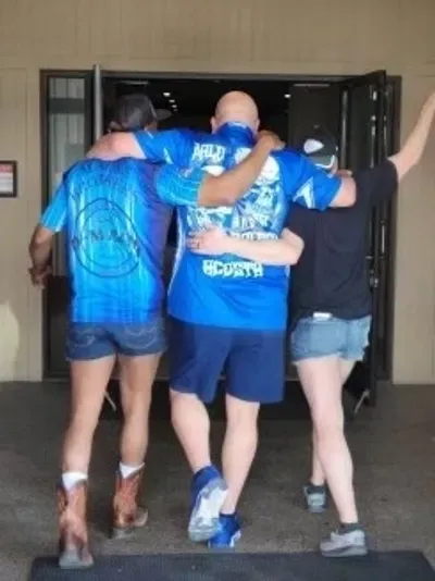 Three people walking arm-in-arm down a hallway, dressed casually.